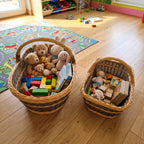 Set of two willow nesting baskets with handles used as toy storage in a children's room, filled with teddy bears and wooden blocks