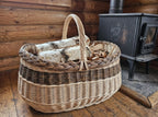 Large oval willow basket with handle used as a log basket for birch firewood beside a wood stove in a log cabin