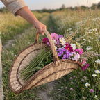 Hand carrying the large wicker flower trug by its tall handle through a wildflower meadow, filled with cut garden flowers
