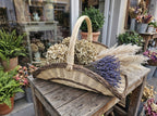 Large wicker flower trug with tall handle holding dried hydrangeas, lavender and pampas grass outside a flower shop