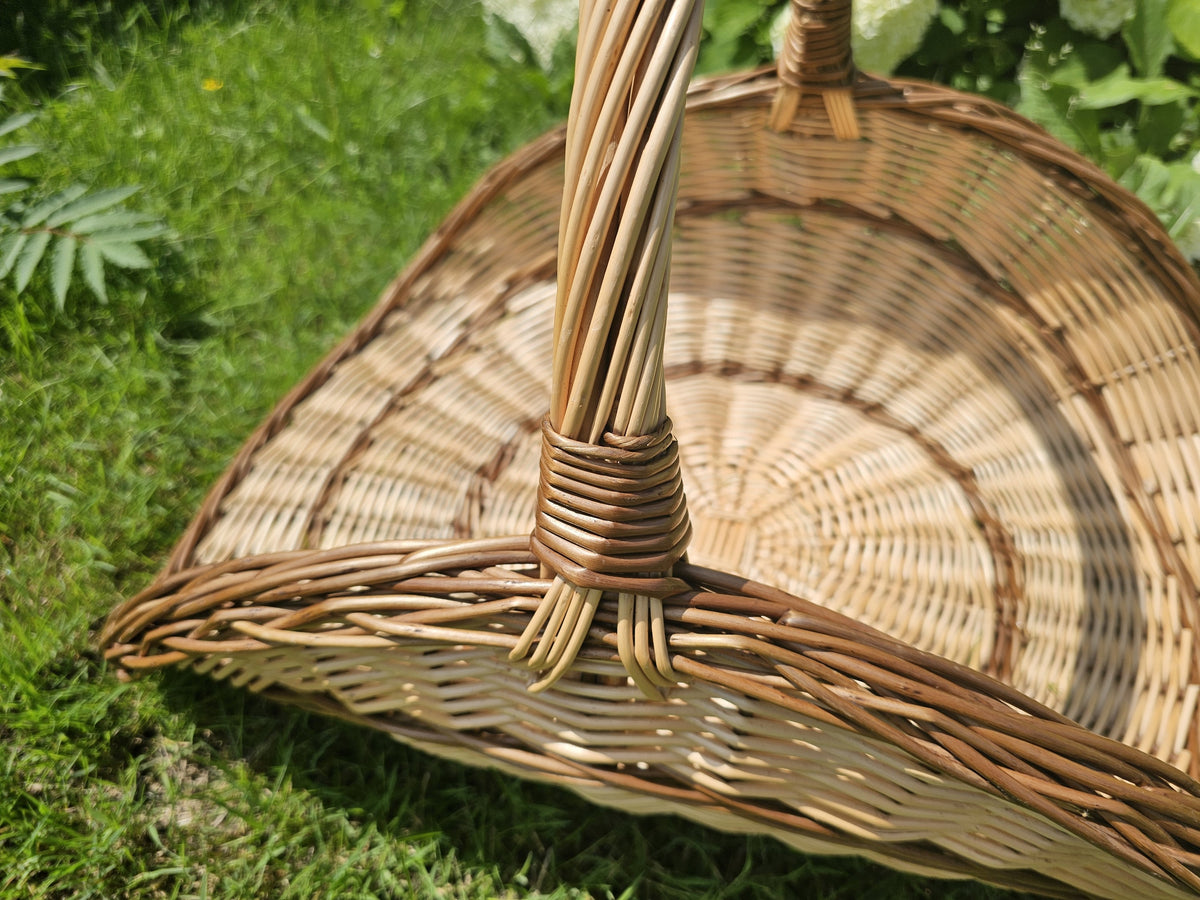 Close-up of the large wicker flower trug on green grass, showing the bound handle and the woven fan-shaped back