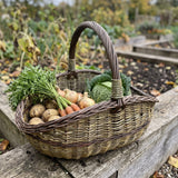 Großer Sammelkorb mit gedrehtem Henkel voller Möhren, Kartoffeln, Zwiebeln und Kohl auf einem Hochbeet