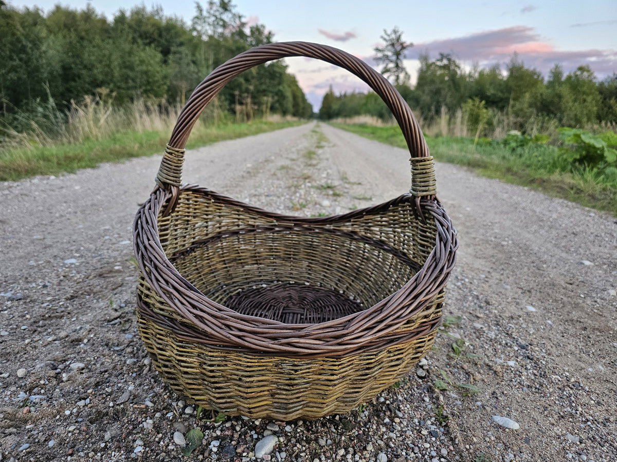 Unpeeled willow basket standing on a gravel road under a pink evening sky.
