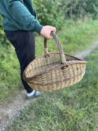 The willow basket carried in one hand by a person walking along the grass verge, showing its size in use.