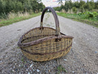 Handwoven willow basket on a gravel road, the arched handle rising from the plaited rim.