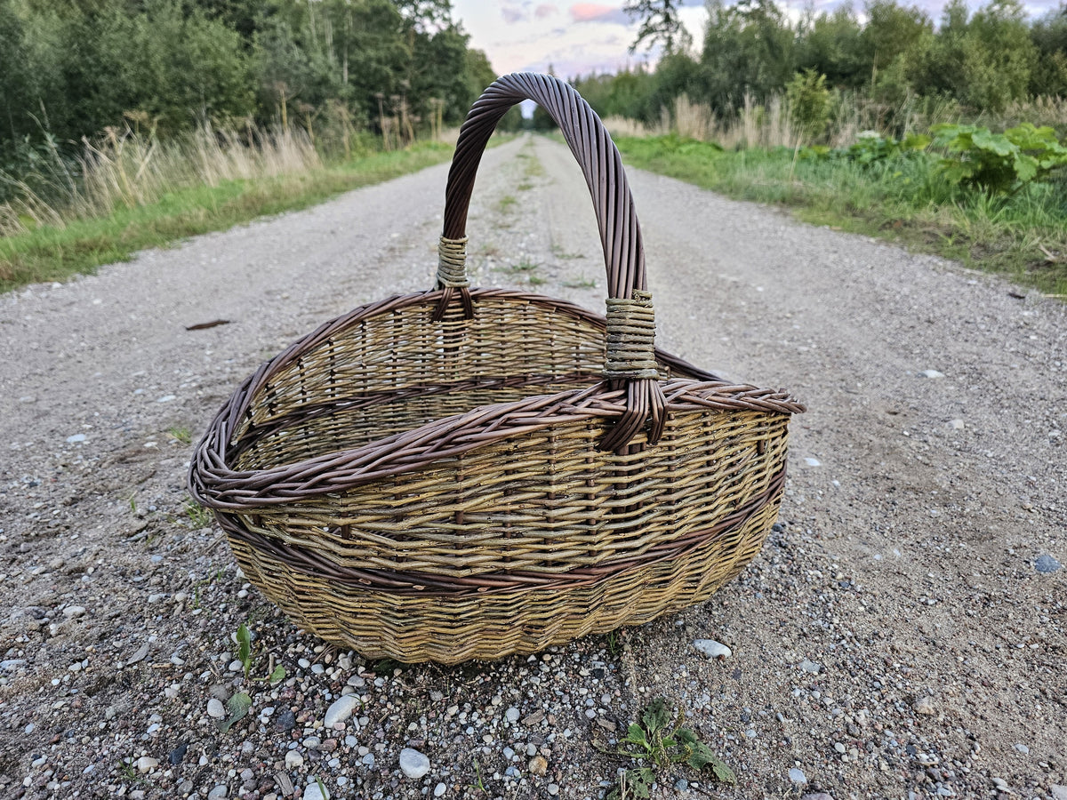 Handwoven willow basket on a gravel road, the arched handle rising from the plaited rim.
