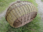 The basket resting on its side in the grass, showing the outer weave and the shaping of the base.