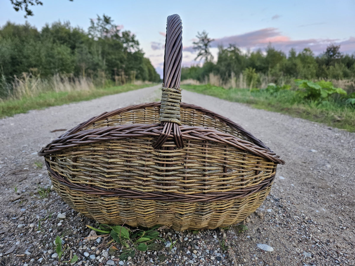 Unpeeled willow gathering basket photographed against an evening sky above a gravel road.