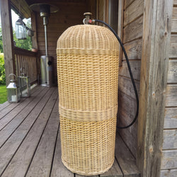 Gas bottle cover for a 50L cylinder, handmade from woven willow, hiding the LPG tank on a wooden terrace with only the valve and hose showing.