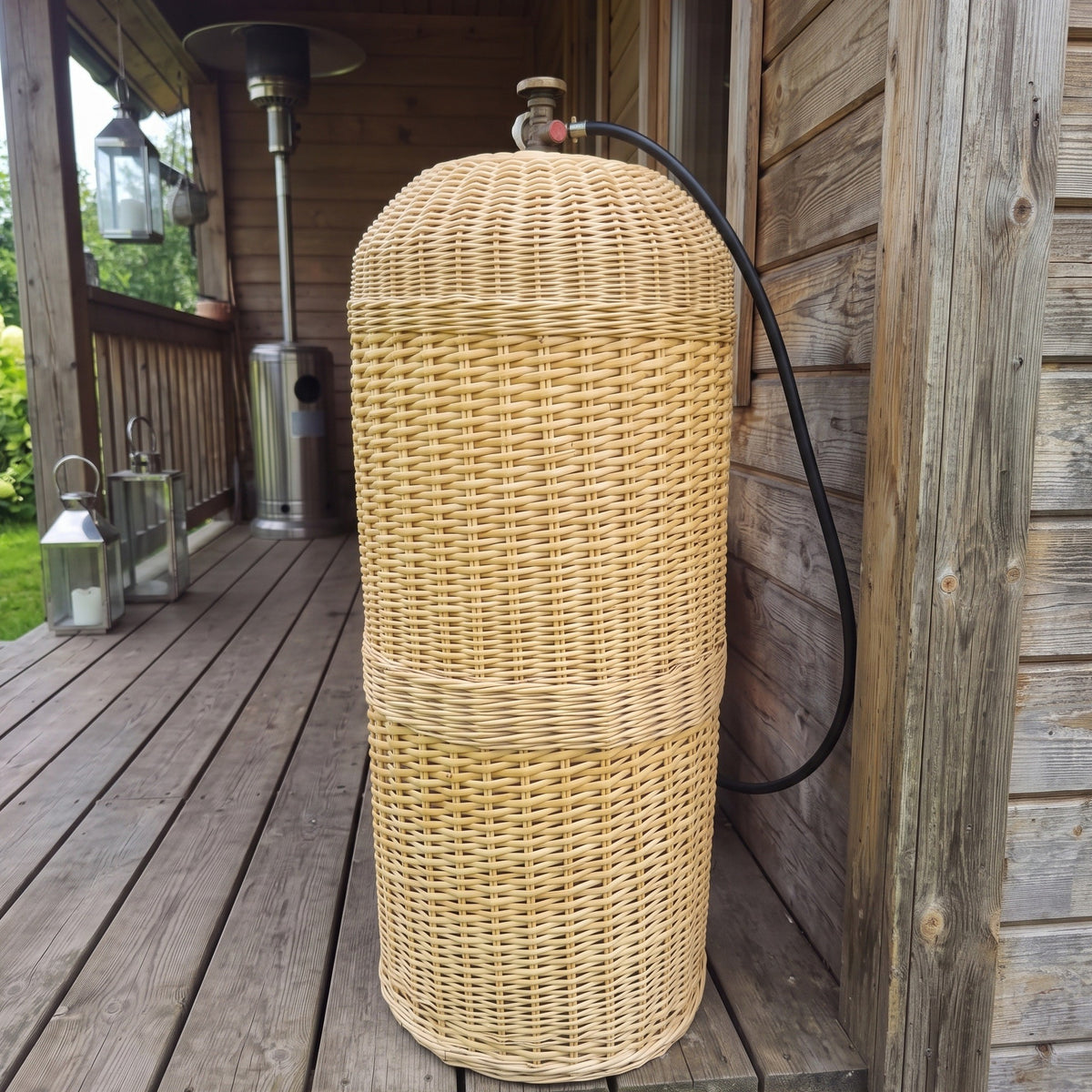 Gas bottle cover for a 50L cylinder, handmade from woven willow, hiding the LPG tank on a wooden terrace with only the valve and hose showing.