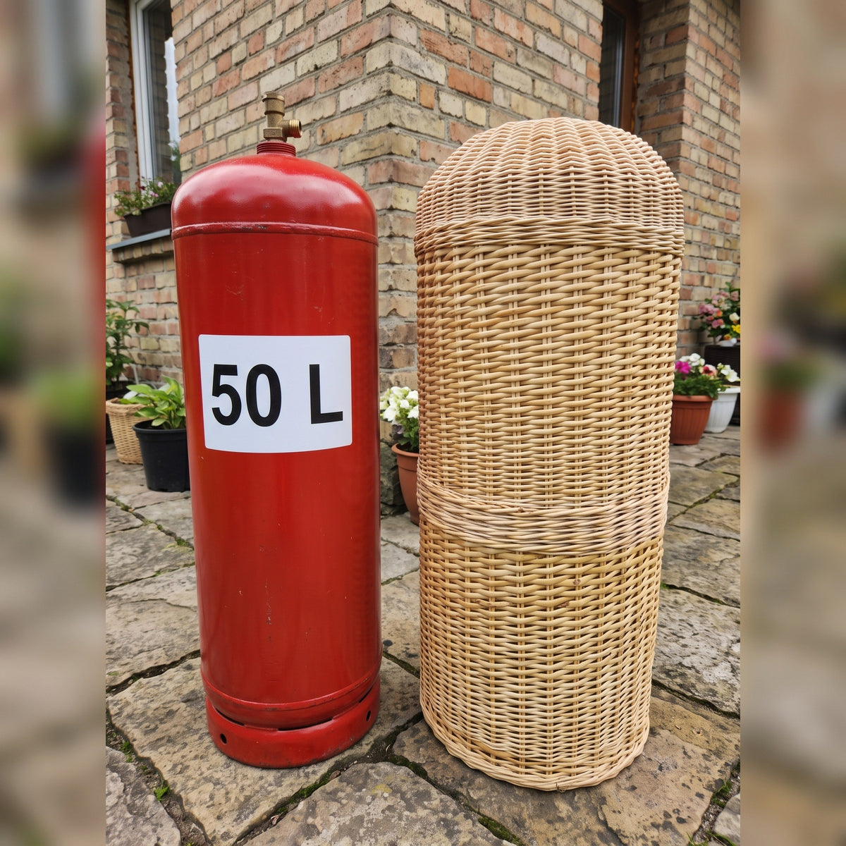 Handwoven wicker LPG sleeve standing next to an uncovered red 50 L gas cylinder in a brick courtyard, showing how the cover hides the tank.