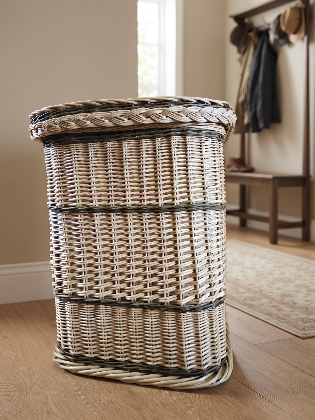 Tall wicker storage hamper with braided lid edge standing in a hallway with a coat rack and bench behind