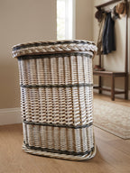 Tall wicker storage hamper with braided lid edge standing in a hallway with a coat rack and bench behind