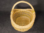 Handwoven willow basket with a sturdy arched handle viewed from the end, showing where the handle is bound into the rim