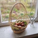 Wicker Easter basket with a tall arched handle and lace-weave sides, holding dyed Easter eggs on moss beside pussy willow on a windowsill