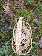 Empty handwoven willow tray with a round base, woven handle and patterned open weave, set on grass and moss in the woods.