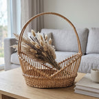 Handwoven willow flower display basket with a tall arched handle and open vertical sides, holding dried bunny tails and lavender by a sofa