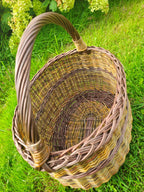 Top view of a tall wicker foraging basket on the lawn, showing the woven base inside and the reinforced arched handle.