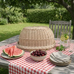 Handwoven bread cloche with tray on a red checked garden picnic table with sliced watermelon, cherries and a jug of water