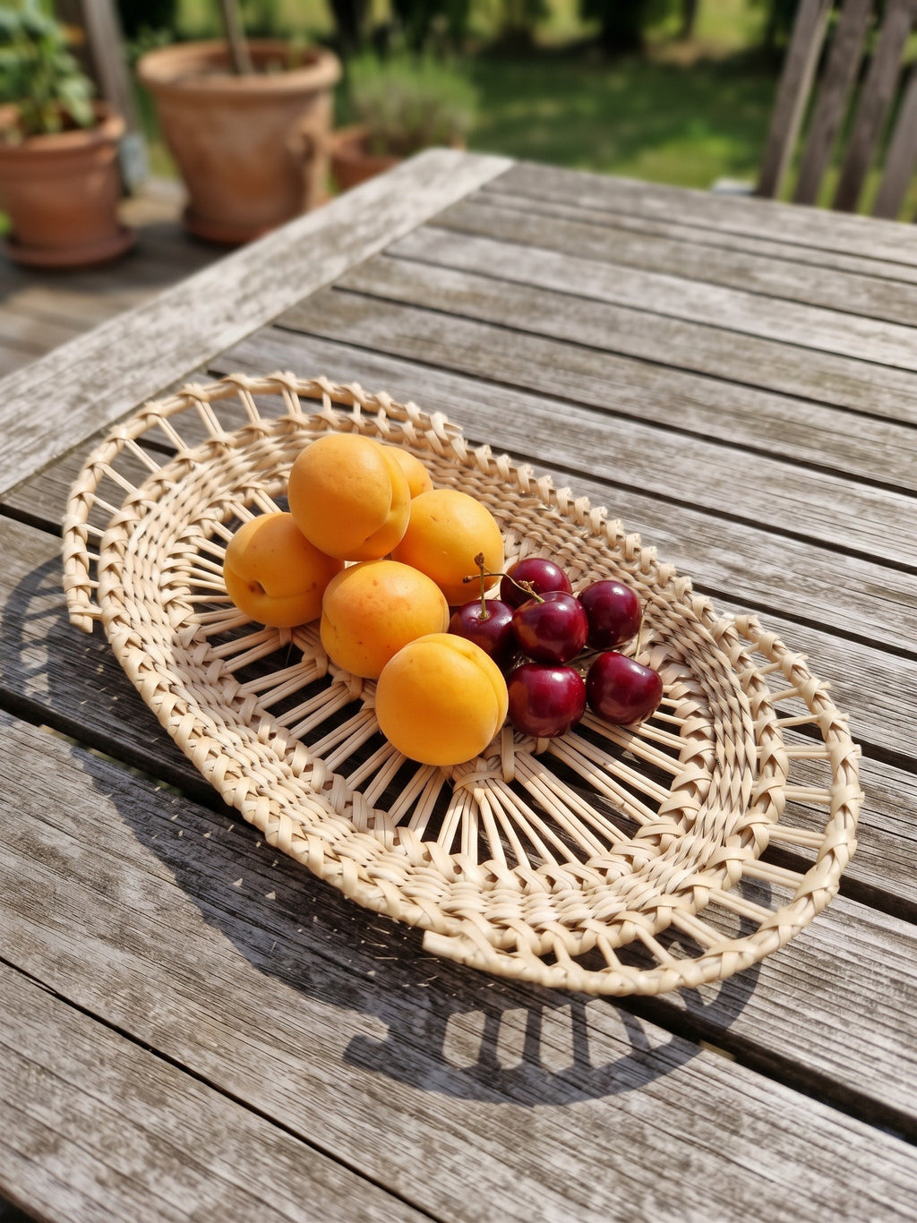 Oval handwoven willow lace-weave platter with apricots and cherries on a weathered garden table, showing the open rings of upright rods.
