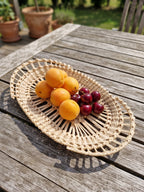 Oval handwoven willow lace-weave platter with apricots and cherries on a weathered garden table, showing the open rings of upright rods.