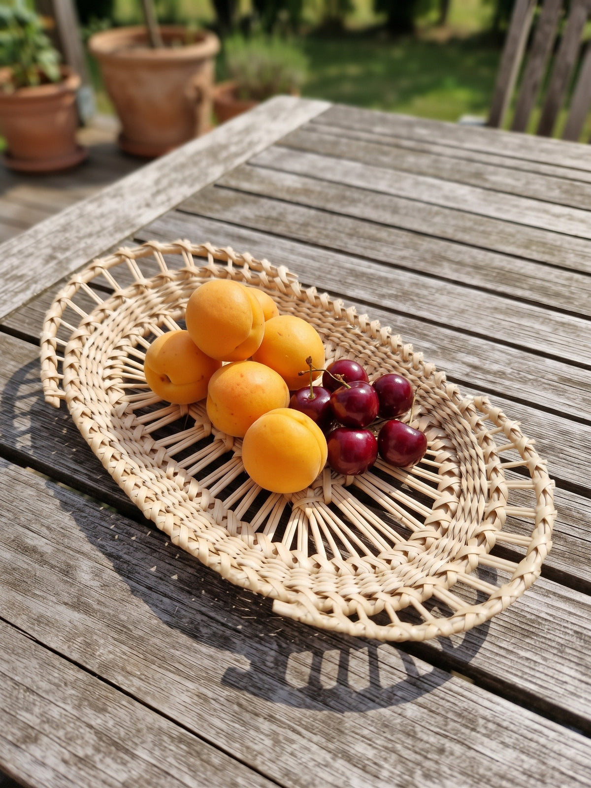 Oval handwoven willow lace-weave platter with apricots and cherries on a weathered garden table, showing the open rings of upright rods.