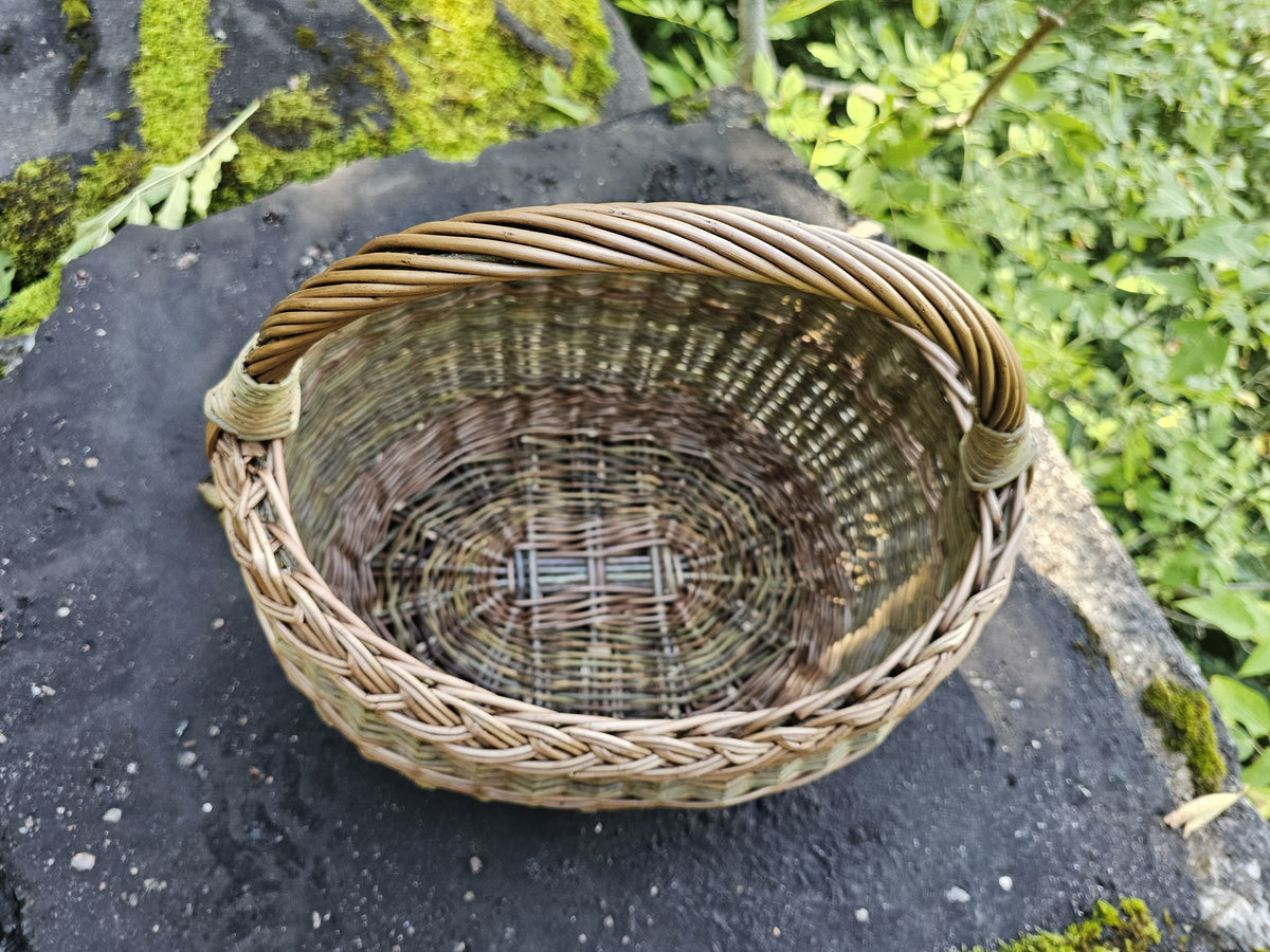 Looking down into a wicker basket on a dark rock, showing the woven oval base and the arched handle bound into the rim.