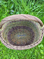 Overhead view in the grass, the plaited rim, the woven collar where the handle joins the side, and the interior all visible at once.