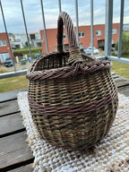 Willow market basket resting on a woven mat on a balcony table, the unpeeled rods and the plaited rim catching daylight.