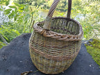 Close view of the willow basket on a dark rock by the river, the thick plaited rim framing the wide oval mouth.