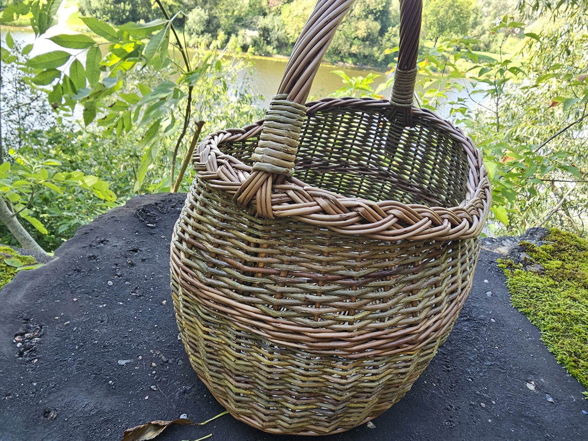 Close view of the willow basket on a dark rock by the river, the thick plaited rim framing the wide oval mouth.