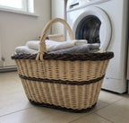 Handwoven willow laundry basket with an arched handle and braided rim, holding folded towels on a tiled floor beside a washing machine