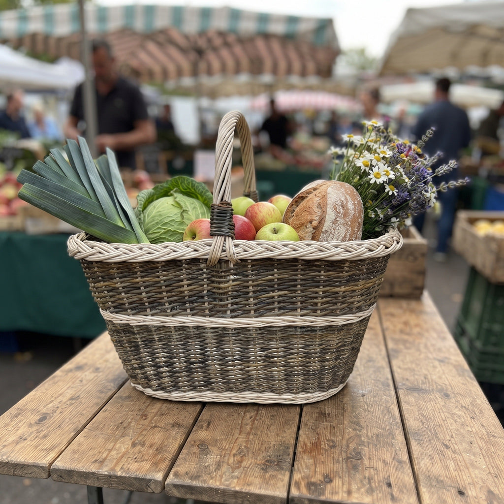 Oval willow market basket with handle carrying leeks, cabbage, apples, bread and wild flowers on a wooden stall at an outdoor market