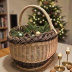 Oval wicker basket with handle filled with pine branches, pinecones and baubles as a holiday gift by a lit Christmas tree