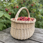 Handwoven egg gathering basket with braided rim filled with fresh raspberries on a garden table beside a raspberry bush