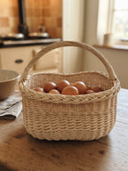 Handwoven egg gathering basket with braided rim filled with fresh hen eggs on a farmhouse kitchen table