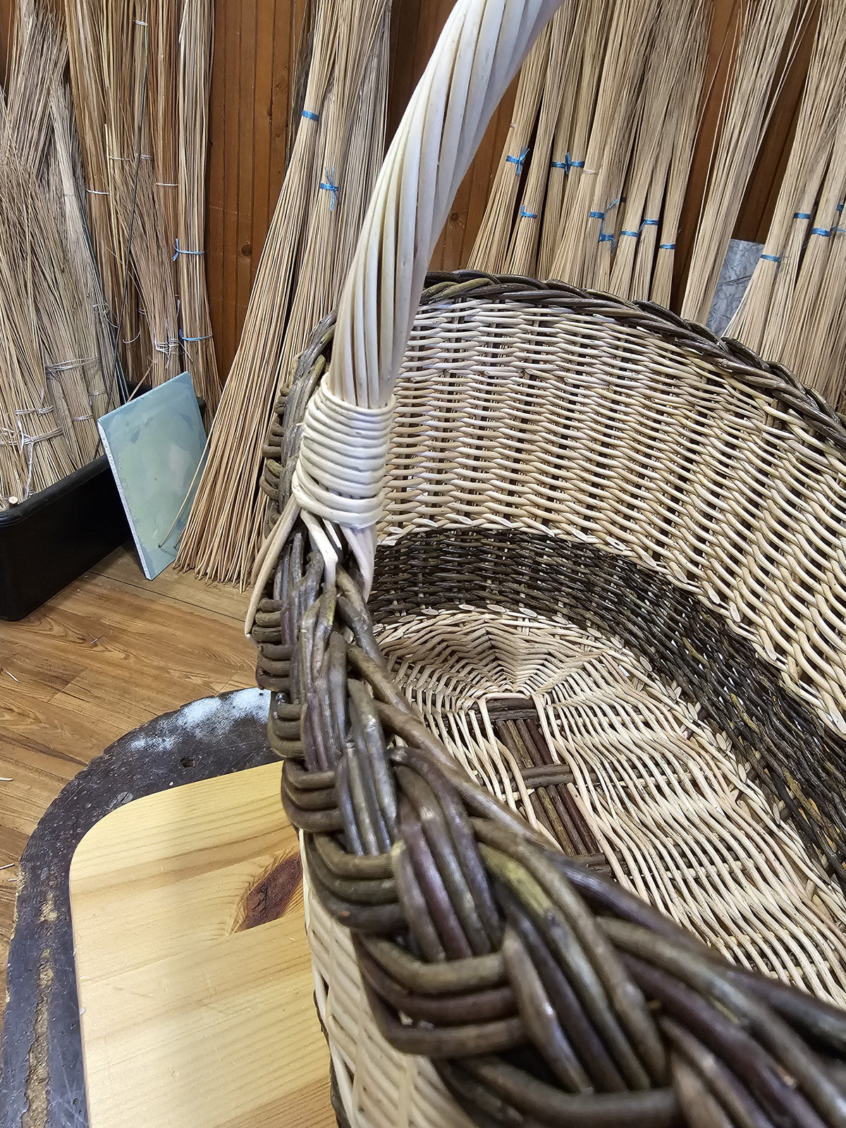 Close-up of the handwoven wicker shopping basket, showing the woven body, the braided rim and the handle tightly wrapped with rods.