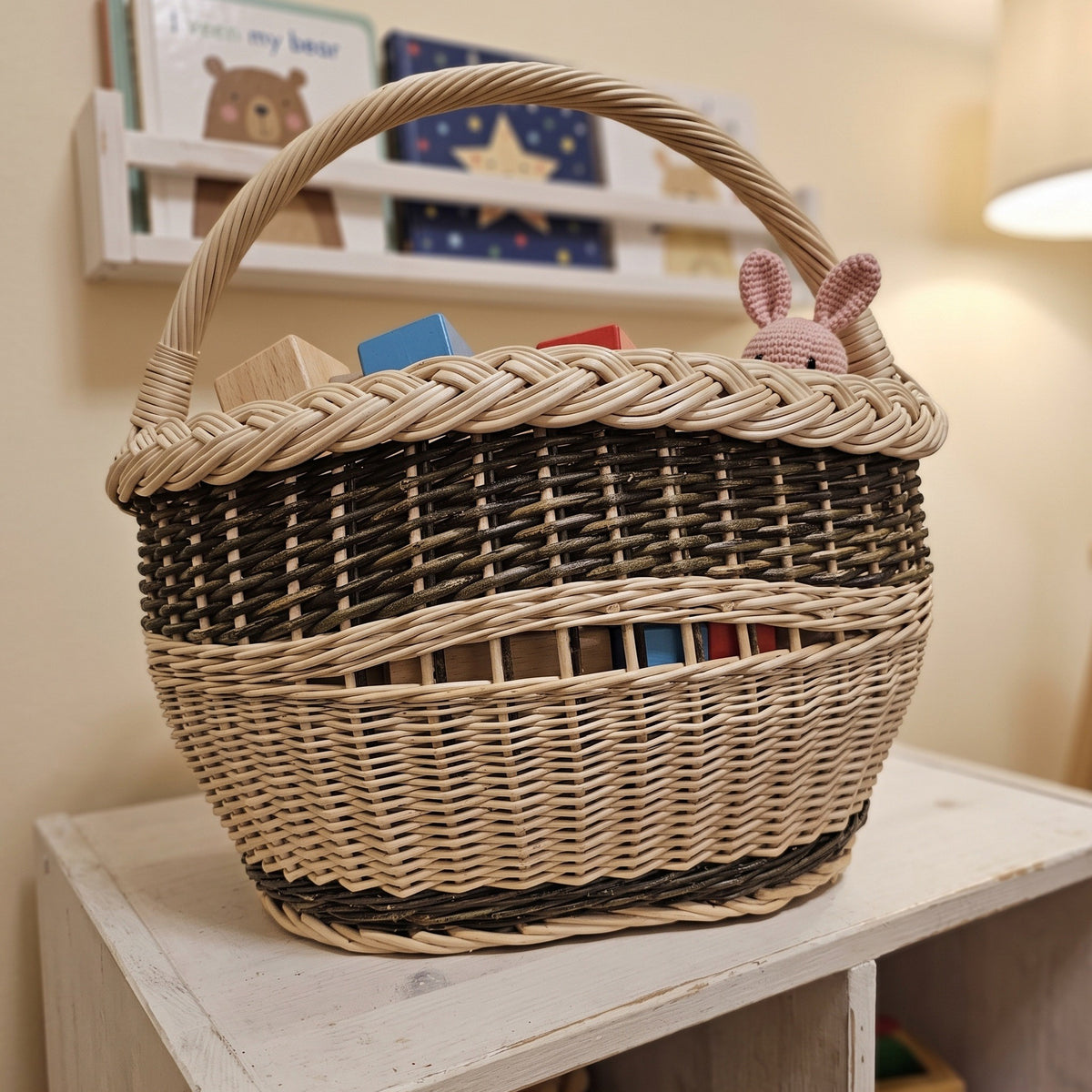 Small willow toy basket with a braided rim and handle filled with wooden blocks and a knitted bunny on a shelf in a nursery