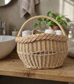 Small wicker storage basket with a braided rim holding rolled towels on a wooden bathroom counter beside a basin