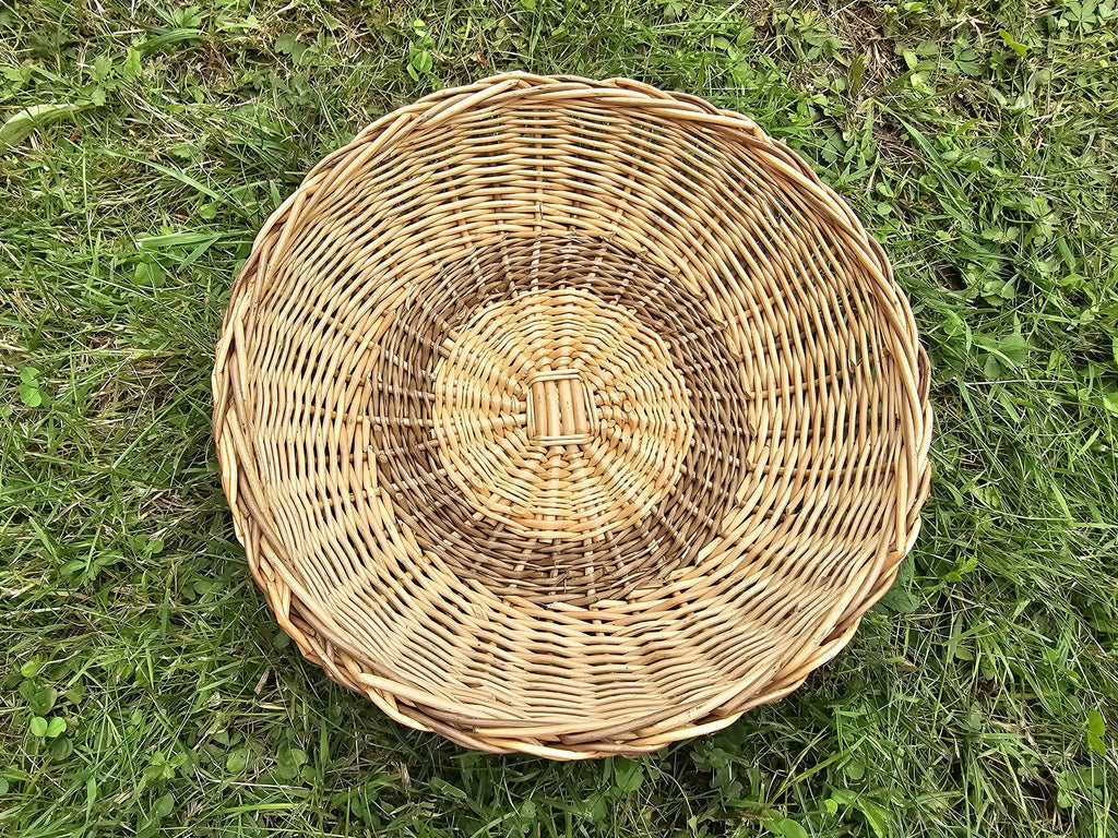 Overhead view of the handwoven willow bread basket on grass, showing the radial weave with a woven inner ring and the braided outer rim.