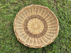 Overhead view of the handwoven willow bread basket on grass, showing the radial weave with a woven inner ring and the braided outer rim.