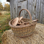Large oval wicker mushroom basket with tall handle filled with parasol mushrooms on a hay bale beside an old wooden barn