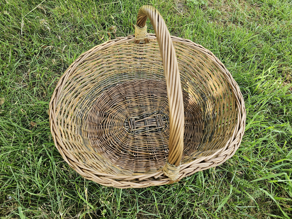 Top view of the large oval willow basket on the grass, showing the woven base, twisted rim and the tall twisted handle