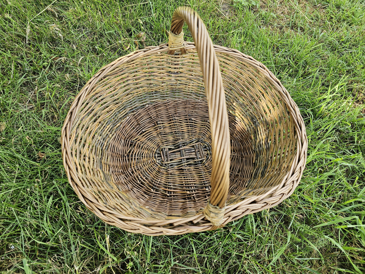 Top view of the large oval willow basket on the grass, showing the woven base, twisted rim and the tall twisted handle