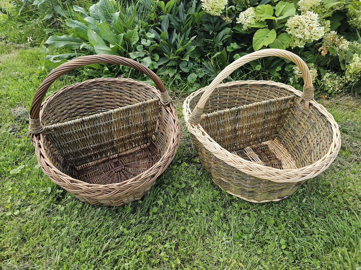Two handwoven willow picnic baskets with dividers side by side on the grass in a garden, showing both available versions.