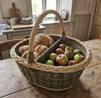 Divided market basket with handle holding sourdough loaves in one compartment and apples and pears in the other on a farmhouse kitchen table