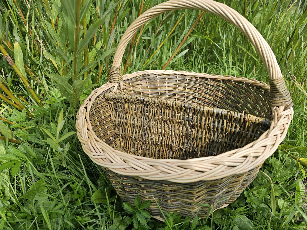 Divided wicker market basket seen from above on long grass, showing both compartments, the braided rim and the arched handle