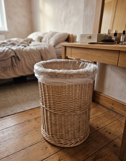 Runder Papierkorb aus Weide mit Müllbeutel auf dem Holzboden neben dem Schminktisch im Schlafzimmer