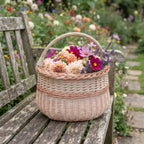 Medium handwoven basket with a braided rim holding a bunch of garden dahlias and cosmos on a wooden bench along a flower garden path