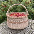 Wicker berry basket with handle filled with fresh raspberries on a garden table in front of raspberry canes